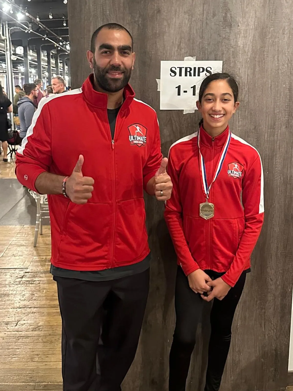 Coach Mahmoud Elshal and young student celebrating at a fencing competition, thumbs up
